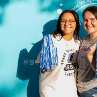 two students posing in front of CAB backdrop at Laker Kickoff photo booth smiling with pom poms